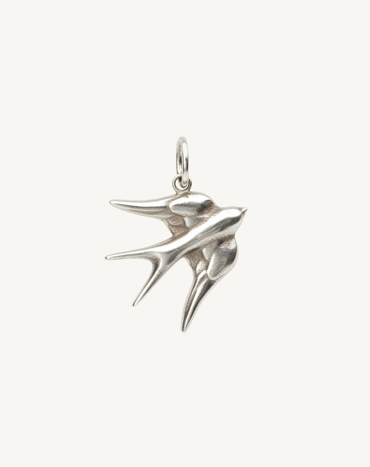 Silver swallow in flight with a jump ring, on a plain cream background