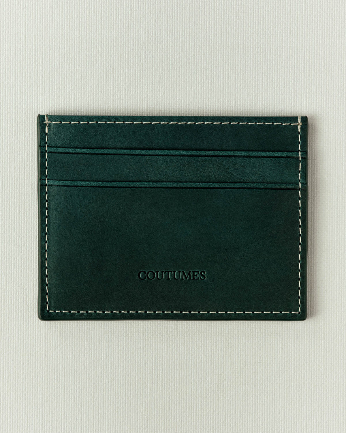 Dark green leather, off-white stitching and an embossed Coutumes logo at the centre