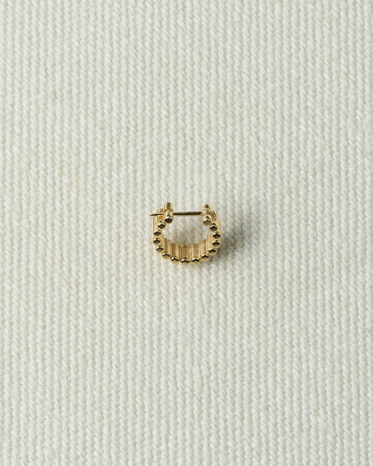 Single gold hoop, ribbed with beaded edges, on textured ecru canvas