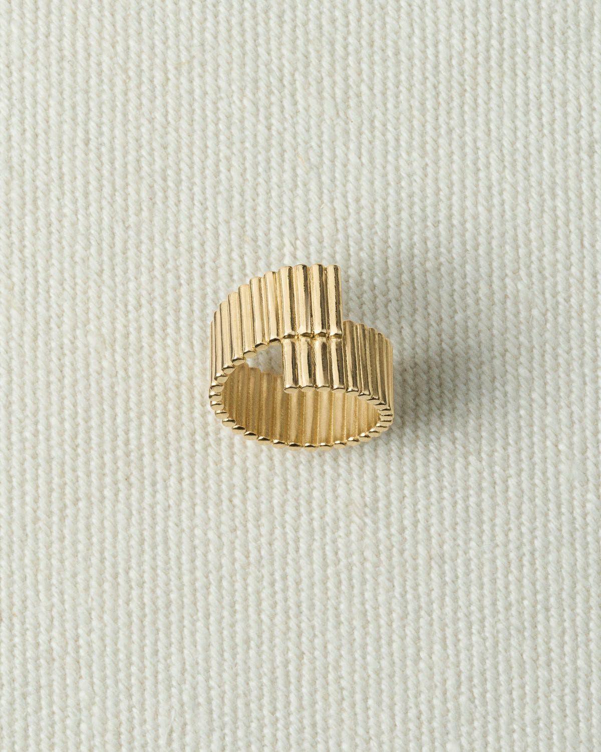 Gold ribbed ring whose ends overlap in a step, seen from above on textured ecru canvas