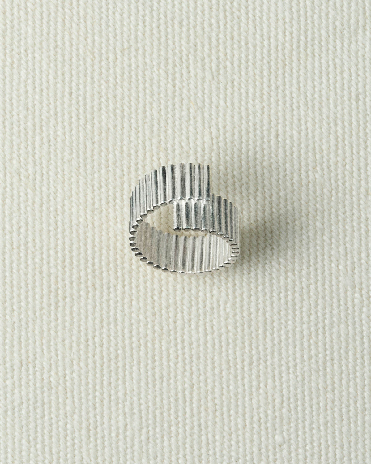 Silver ribbed ring whose ends overlap in a step, seen from above on textured ecru canvas