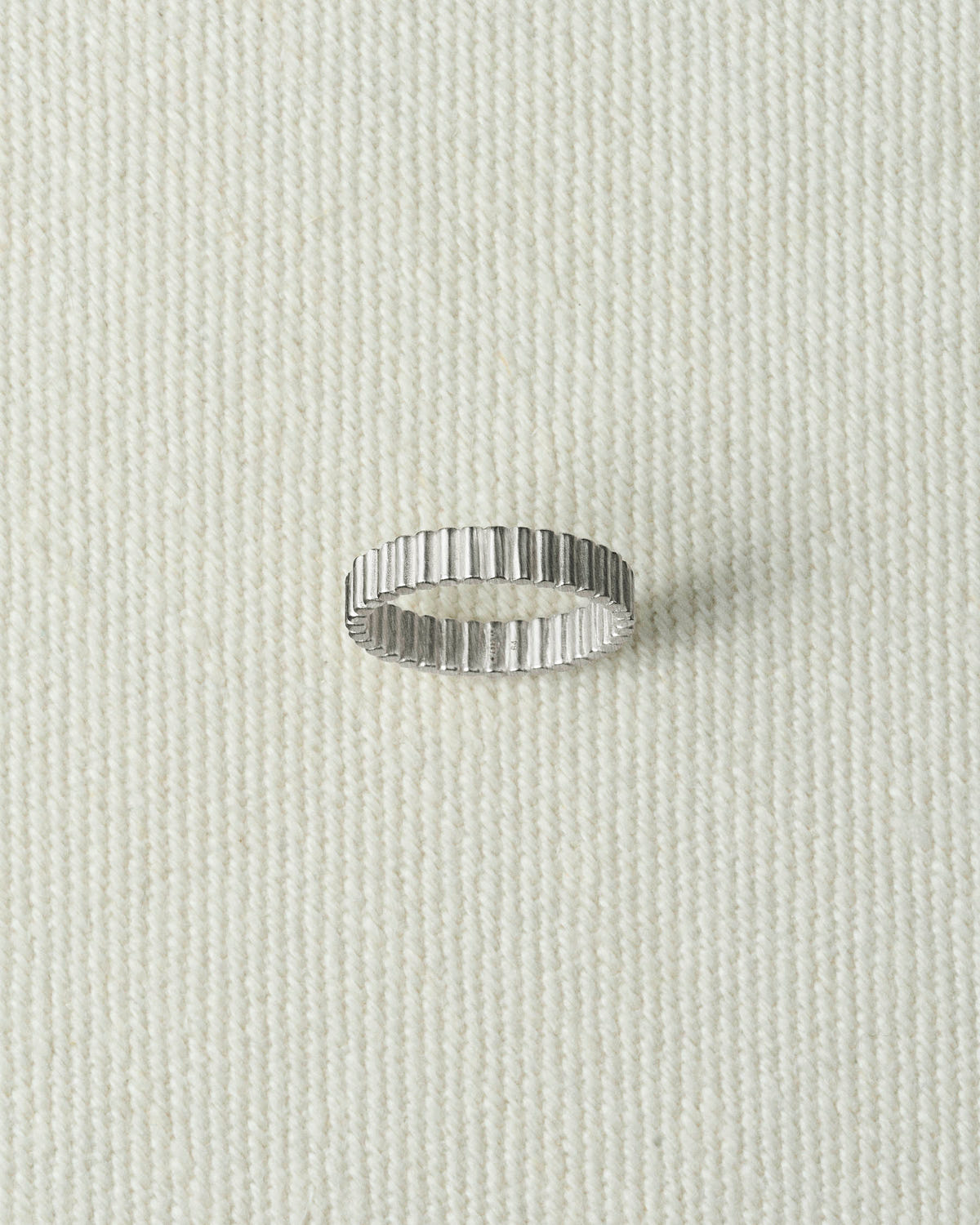 Narrow silver ribbed band lying flat on textured ecru canvas