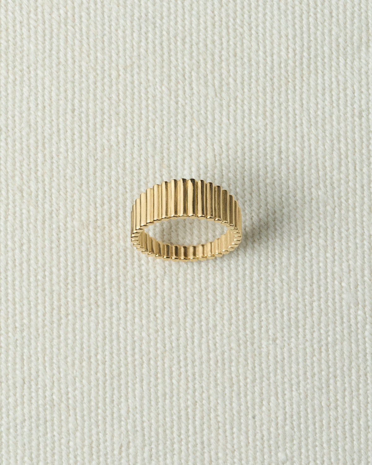Gold ribbed band lying flat on textured ecru canvas