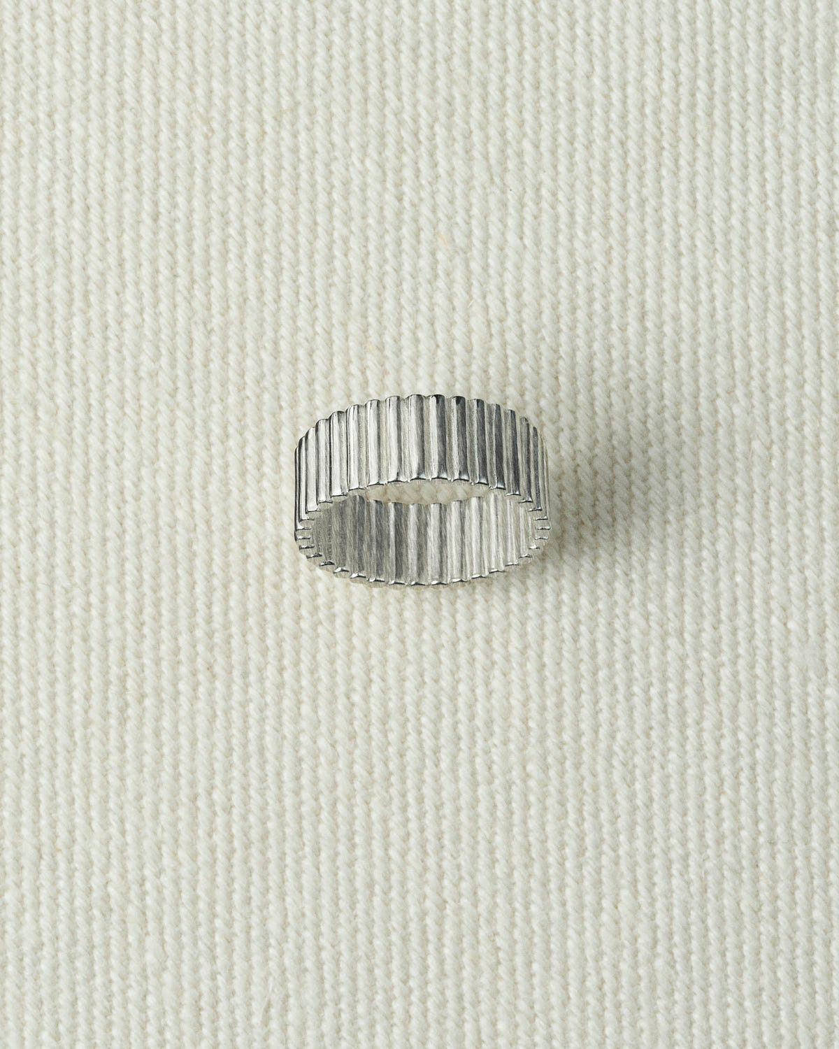 Wide silver ribbed band lying flat on textured ecru canvas