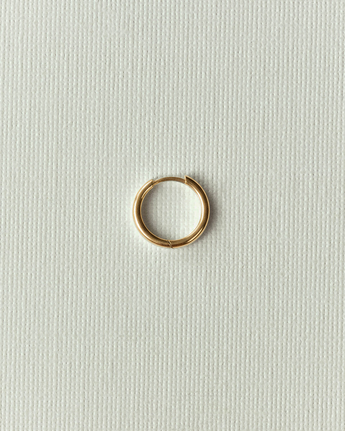 The same ring in gold, alone on textured off-white canvas