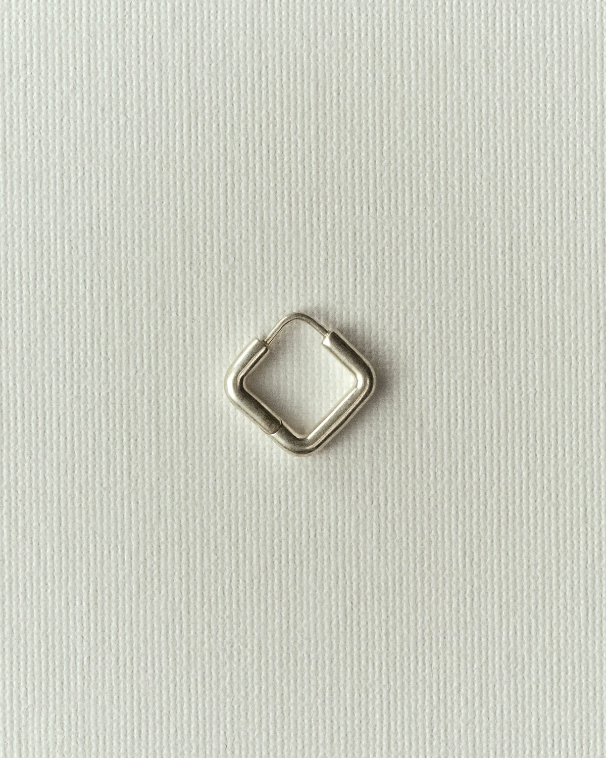 Small square silver hoop with integrated clasp, on off-white textured paper