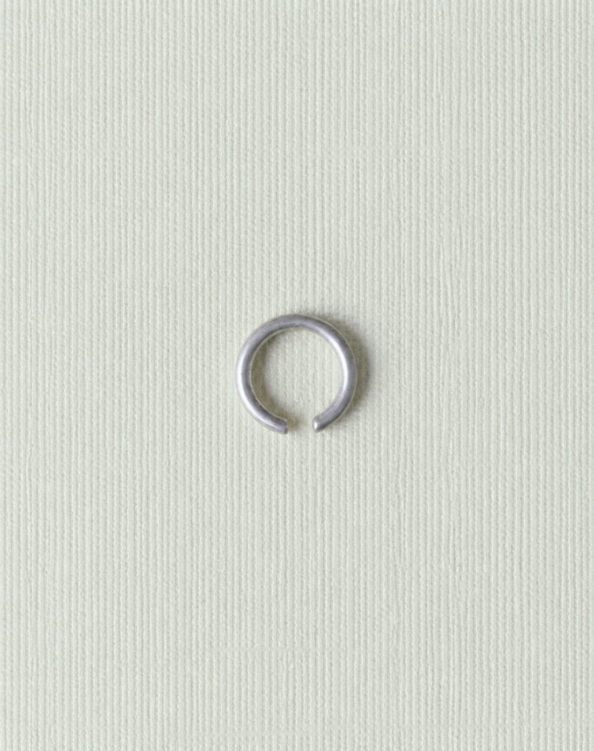 The same open ring in matte silver, close up on pale grey