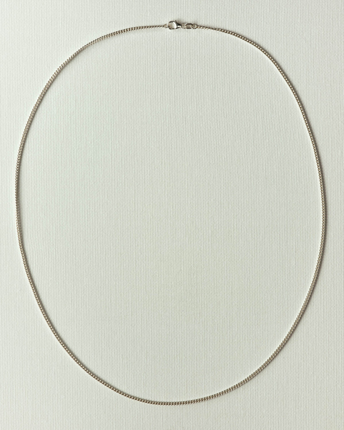 Very fine silver curb links laid in an oval on off-white textured paper