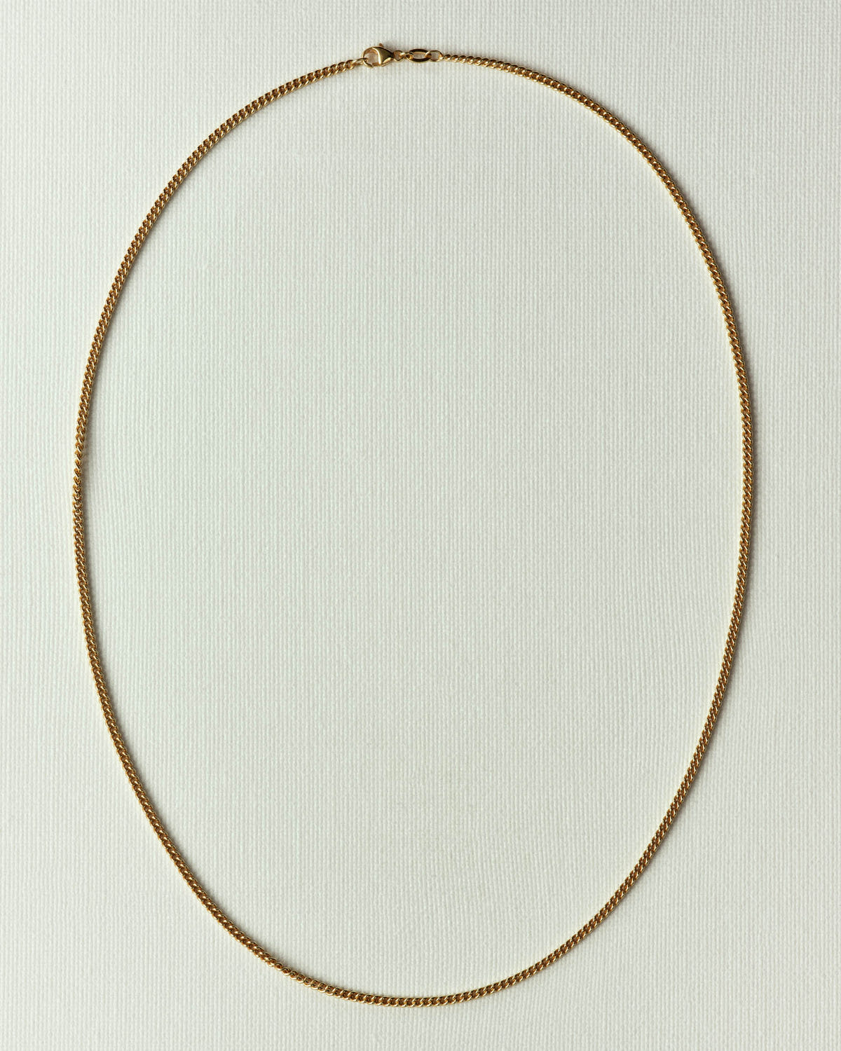The same in gold, lobster clasp at the top, flat on off-white paper