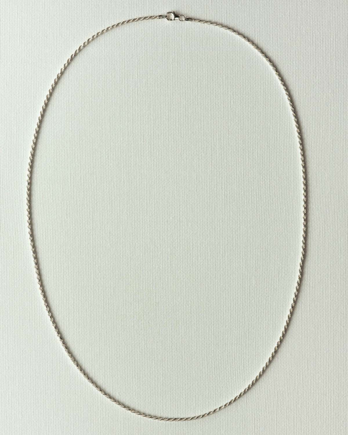 Twisted silver rope links in an oval loop, flat on textured off-white paper