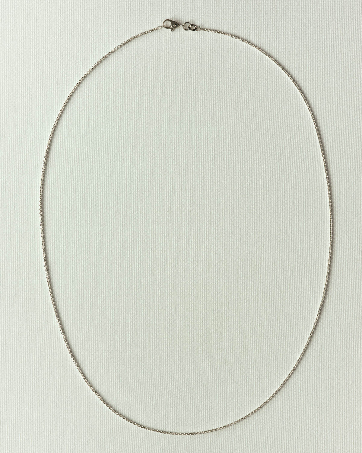 Very fine silver chain looped into an oval, lobster clasp, on textured off-white paper