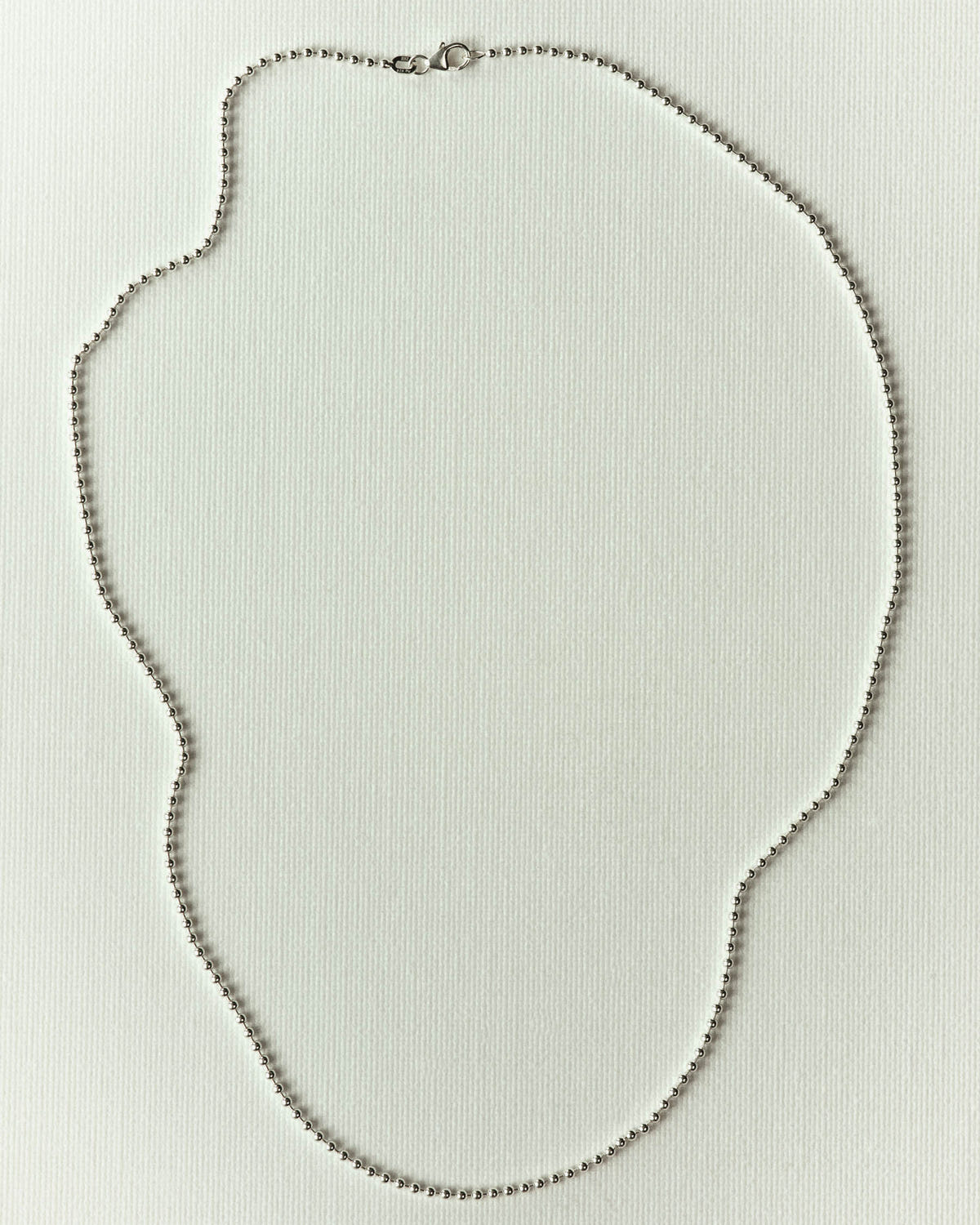 Fine silver ball chain arranged in a loop, lobster clasp, on off-white paper