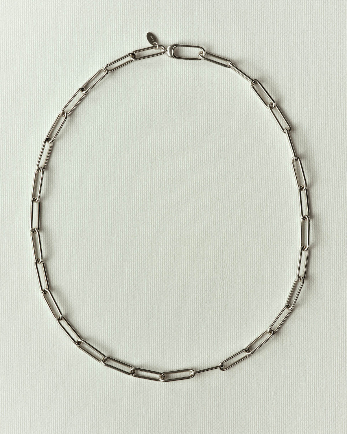 Silver rectangular links and lobster clasp, laid flat on textured off-white paper