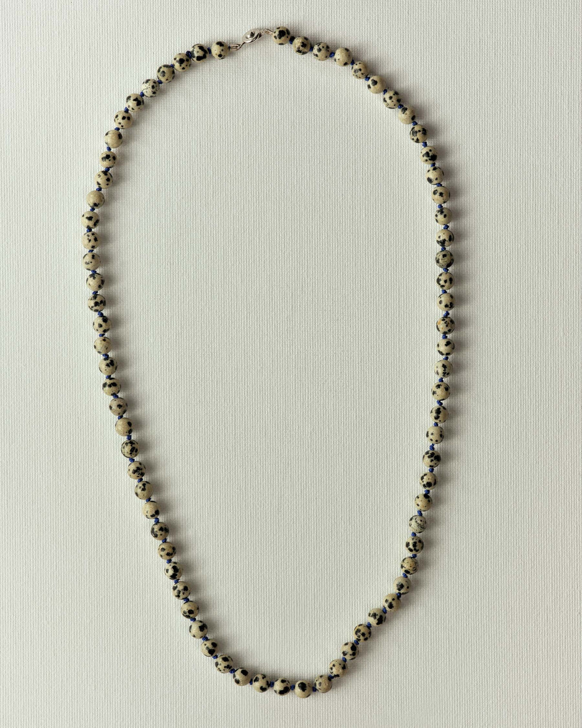 Strand of cream beads flecked with black, silver clasp, flat on textured paper