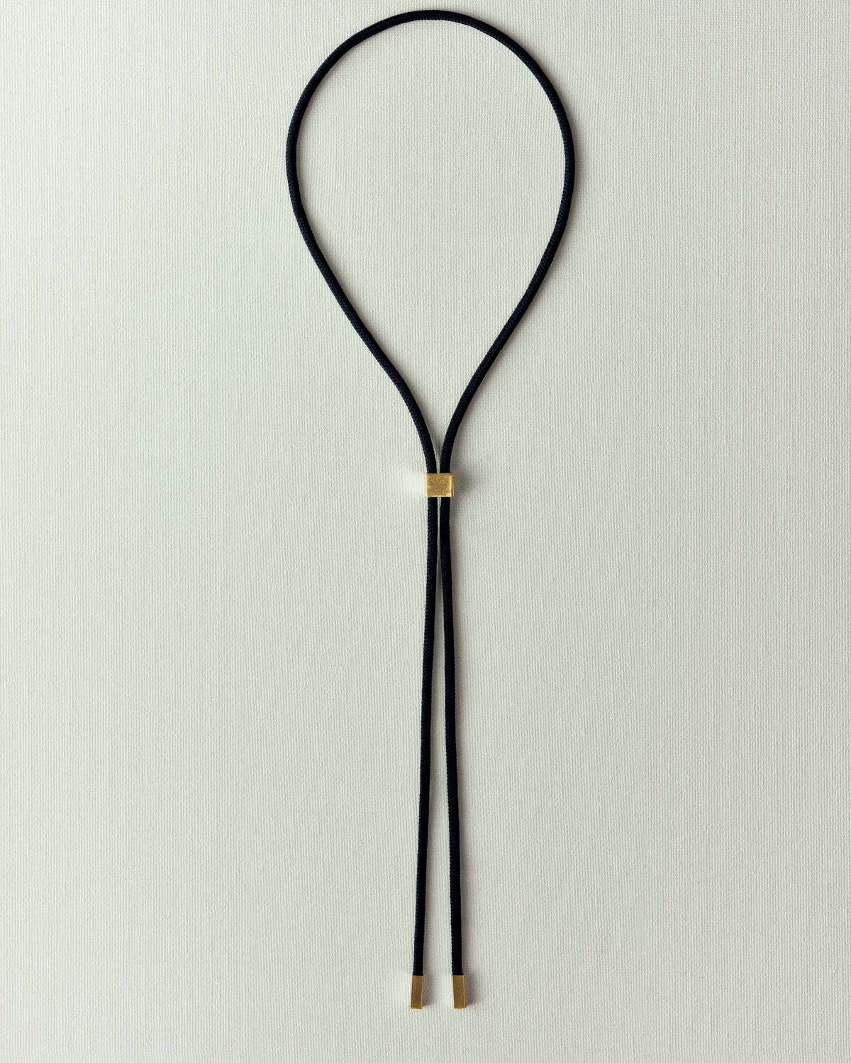 Black braided cord laid flat, square gold slider and tips, cream paper