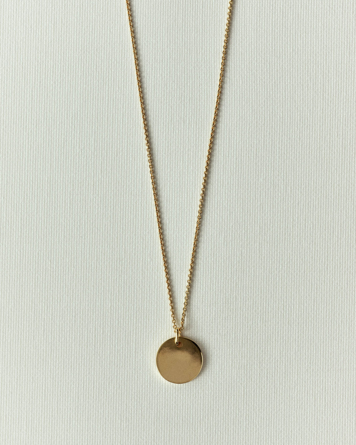 The same piece in gold on a finer chain, flat on off-white paper