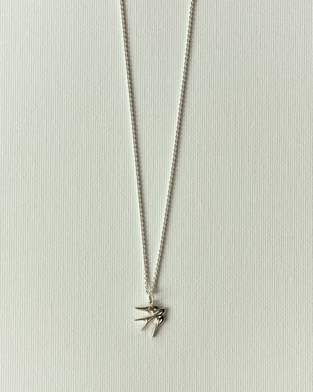 Fine silver chain with a small bird charm, wings spread