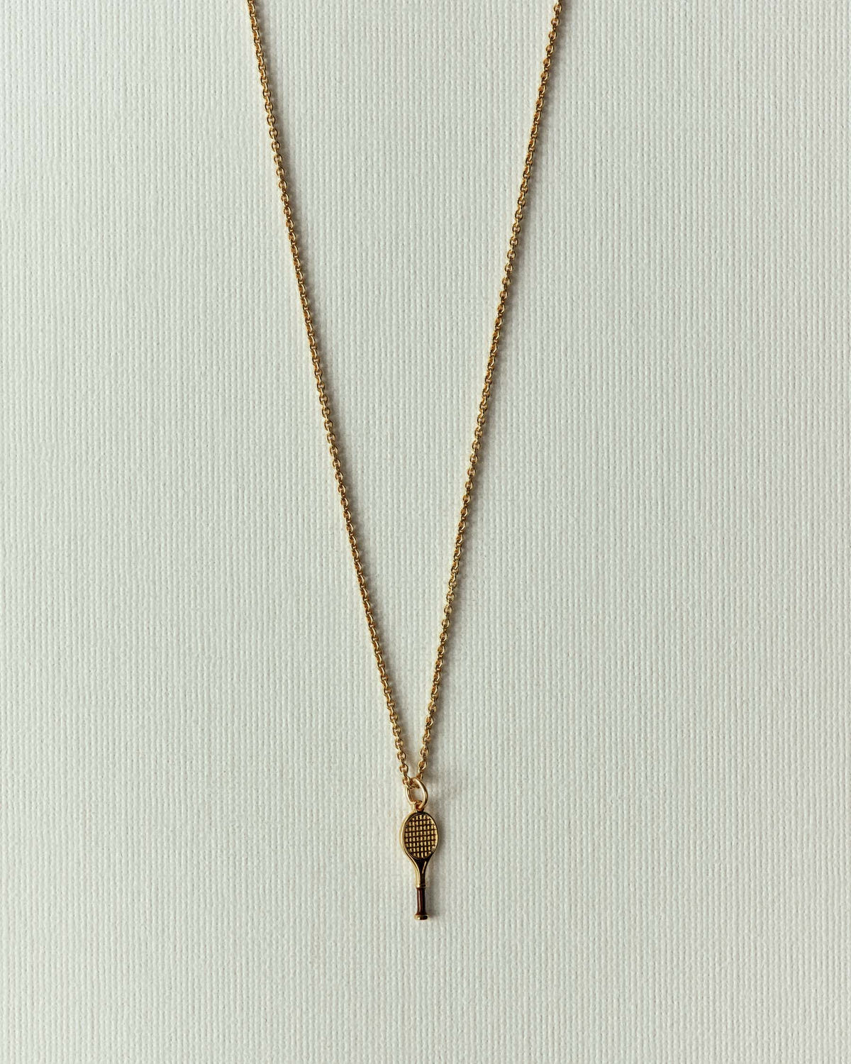 The same racket in gold, fine chain tracing a long V