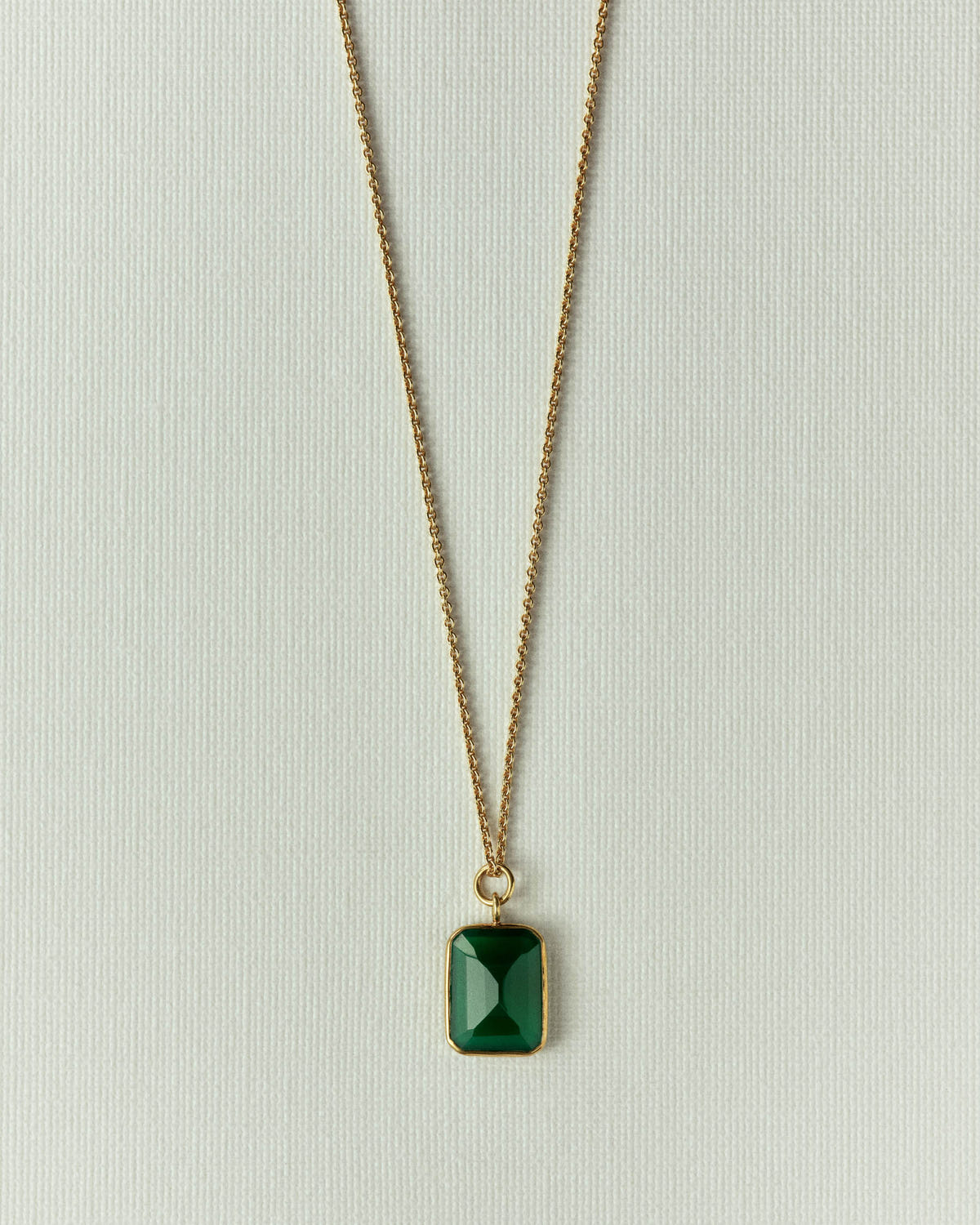 Fine gold chain with a faceted green stone pendant, on textured off-white paper