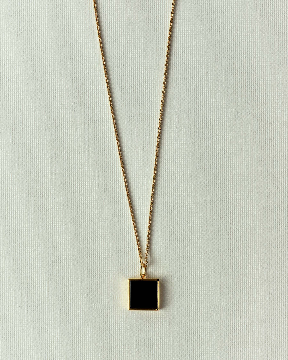 Carré doré serti d'une pierre noire mate, chaîne dorée sur fond écru