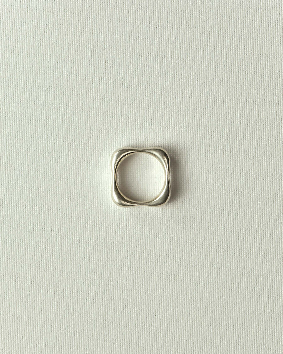 Square band with wavy edges in matte silver, flat on textured ecru canvas