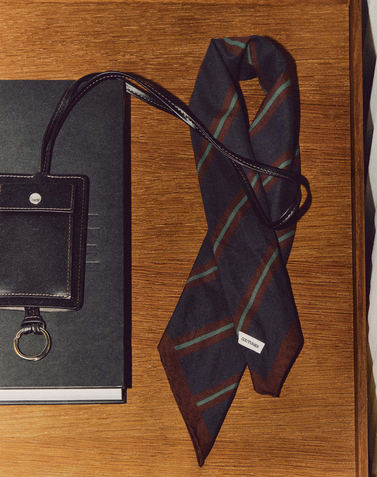 Draped on a wooden table beside a black notebook and a leather case