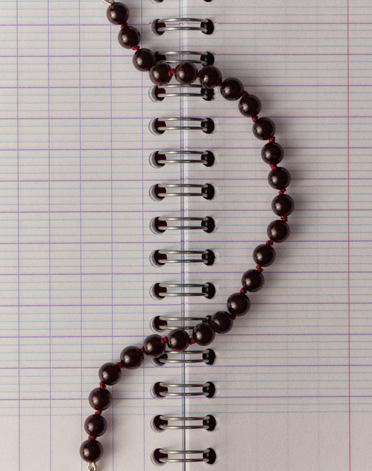 Close-up of dark garnet beads knotted on red thread over a lined notebook