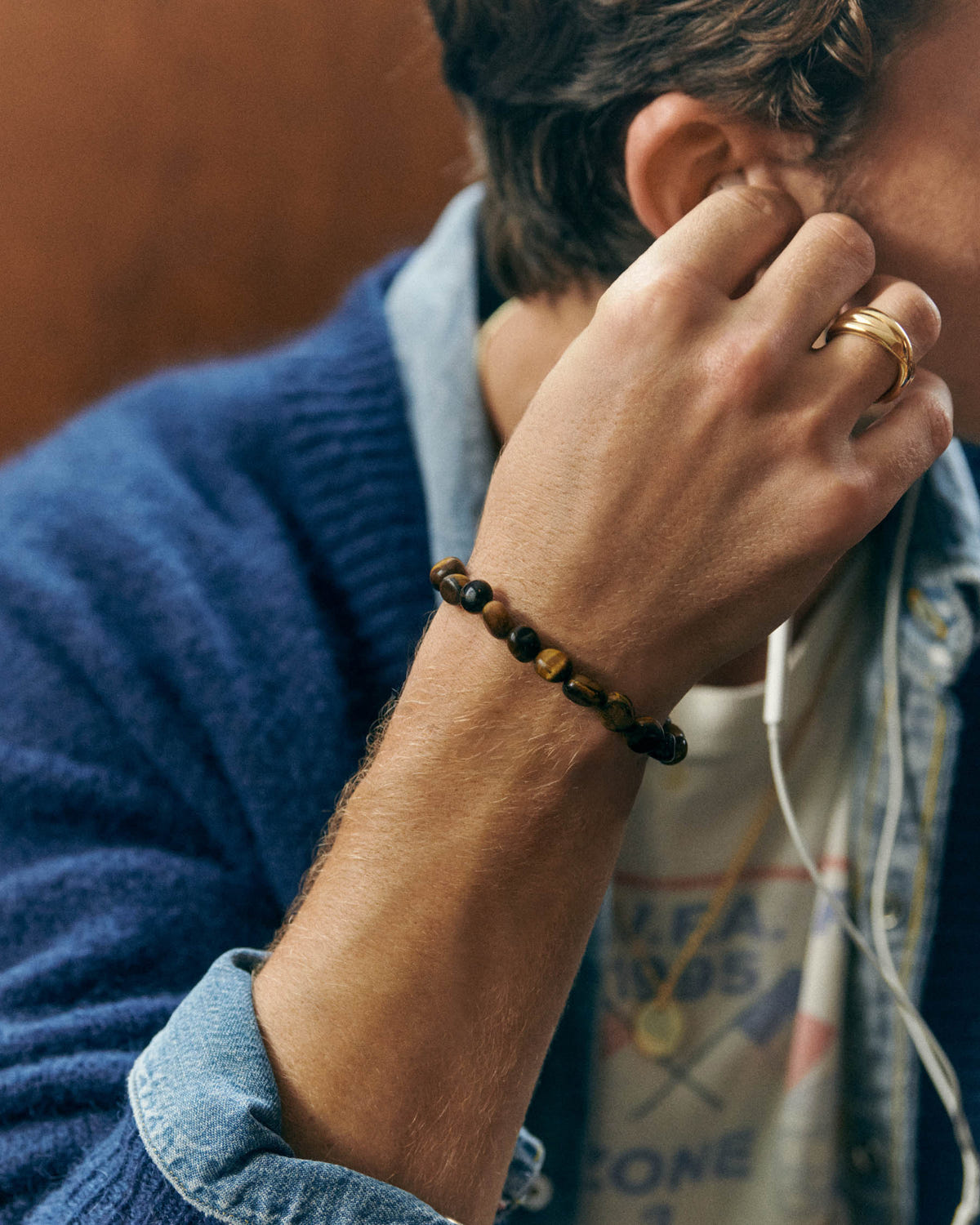 Porté au poignet, main relevée près de l'oreille, gilet bleu sur chemise en jean