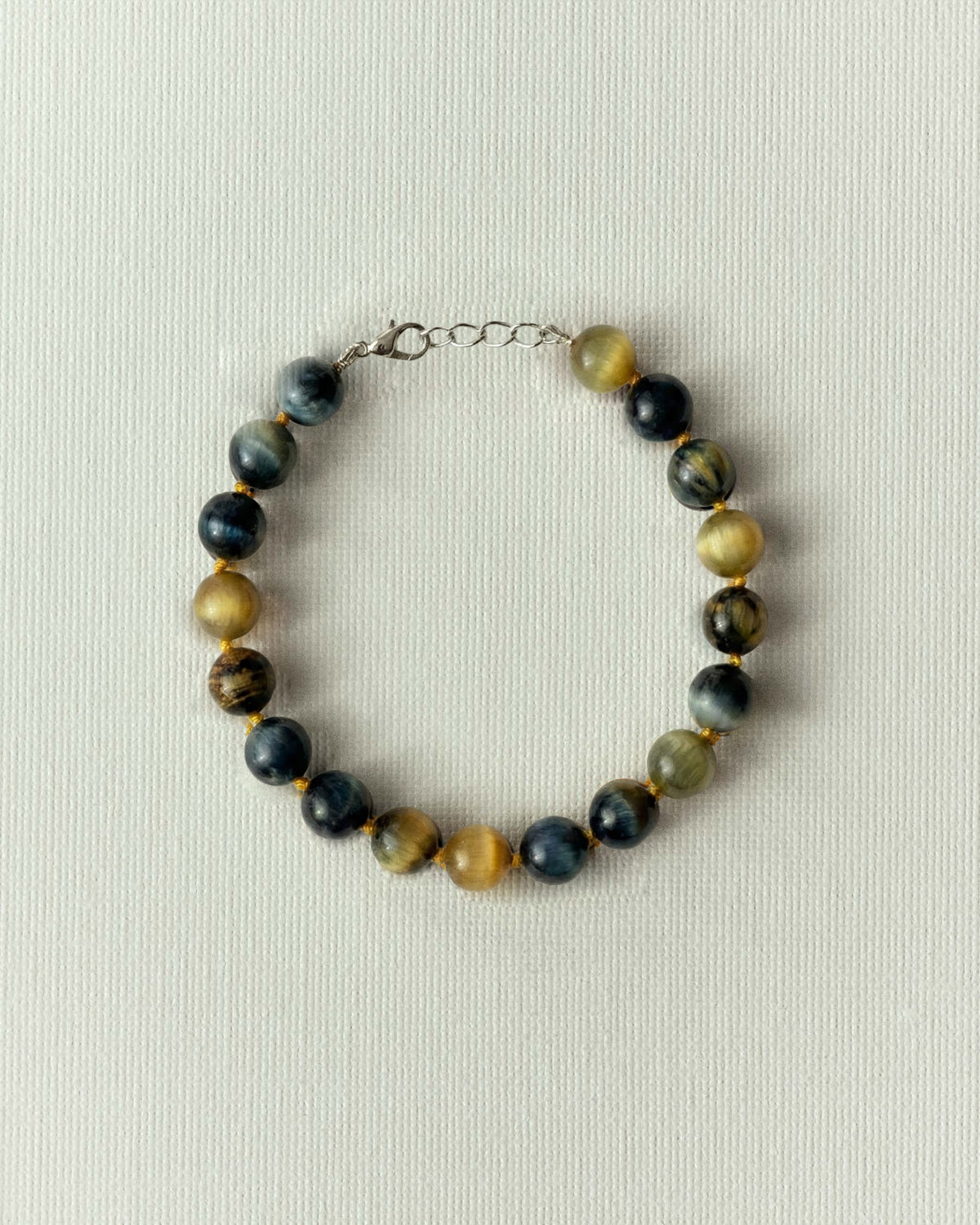 Blue and gold tiger's eye beads, yellow thread between each, silver clasp